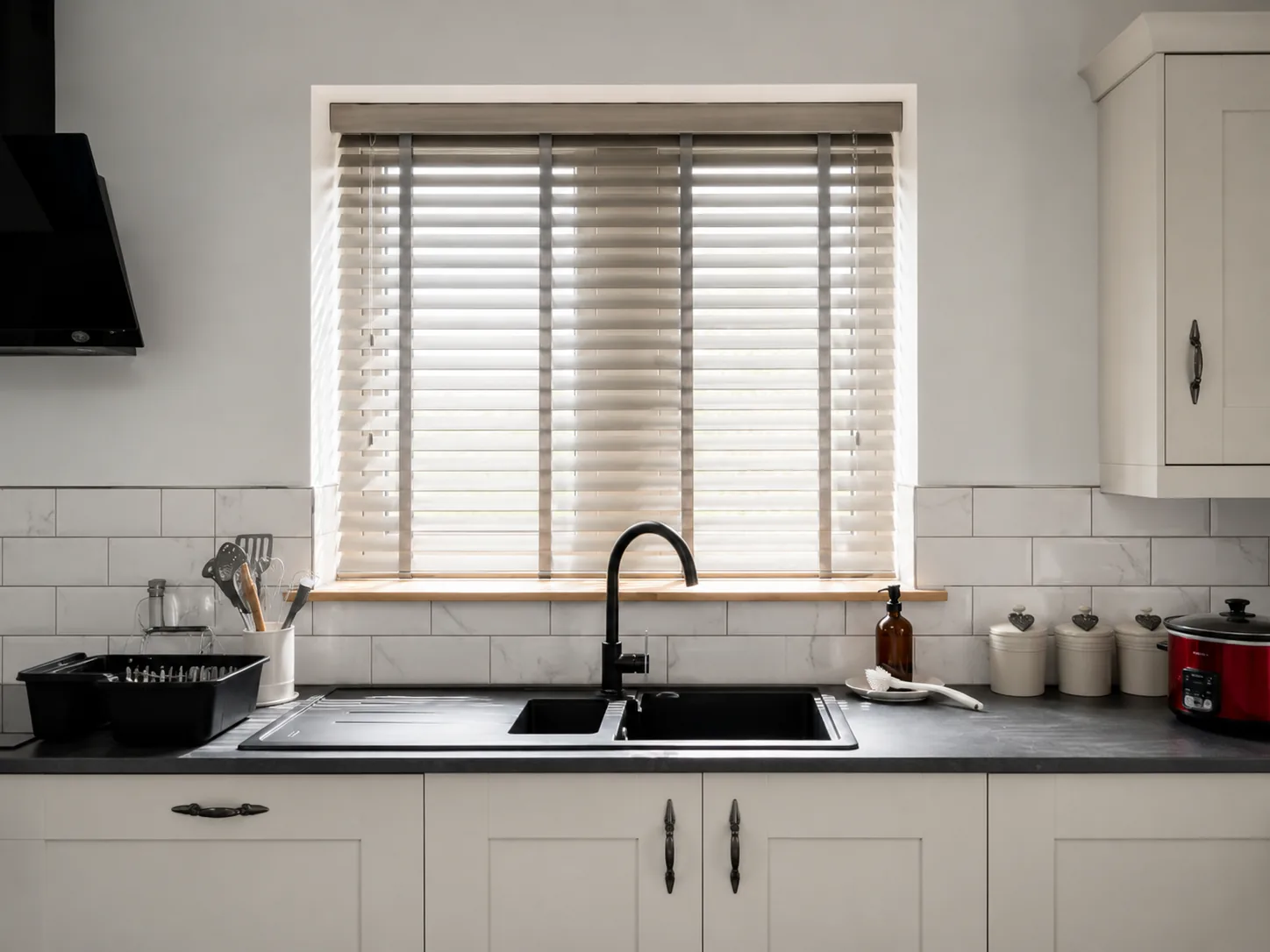 Light Venetian blinds fitted above a black sink in a modern white kitchen