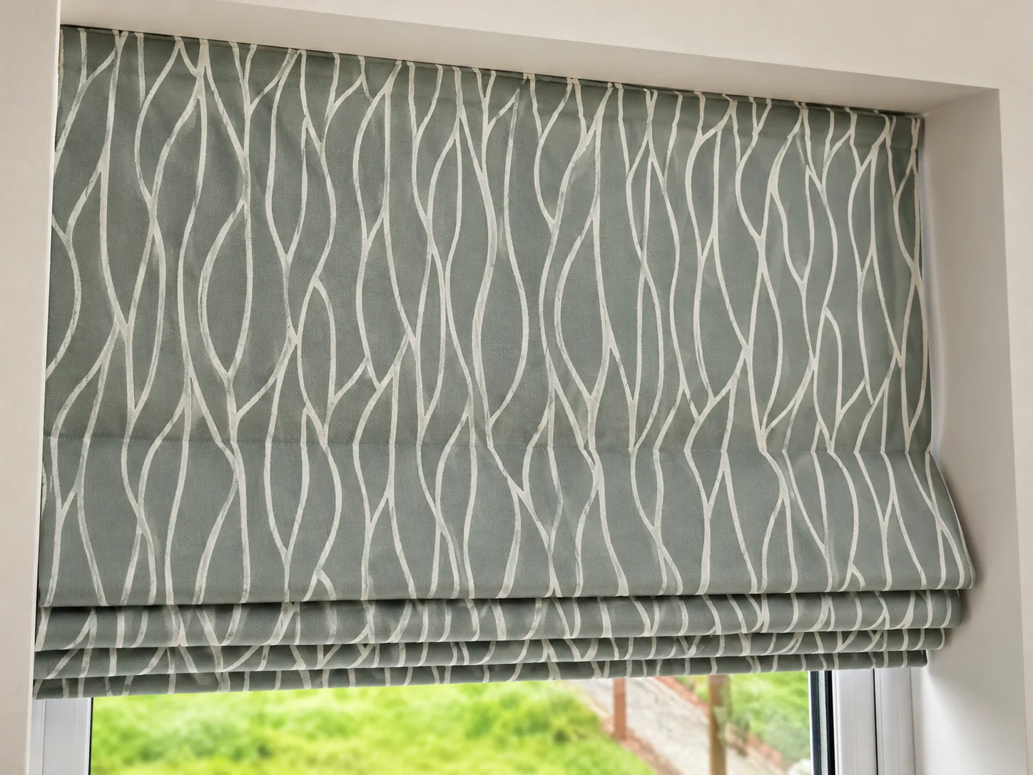 Sage-grey patterned Roman blind with neat fabric folds inside a window recess