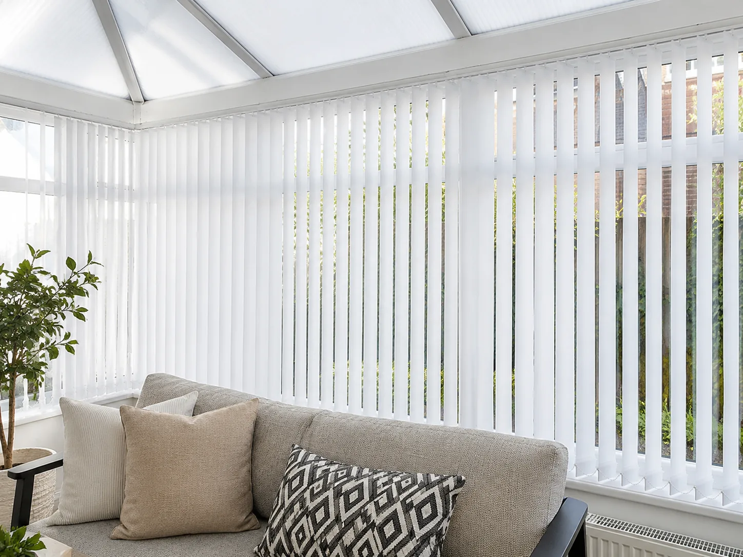 White vertical blinds fitted around the glazing of a bright conservatory